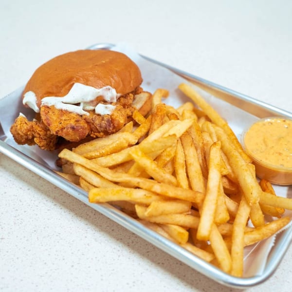Ali's Chicken & Waffles' fried chicken sandwich with white sauce, fries, and dipping sauce on a tray.