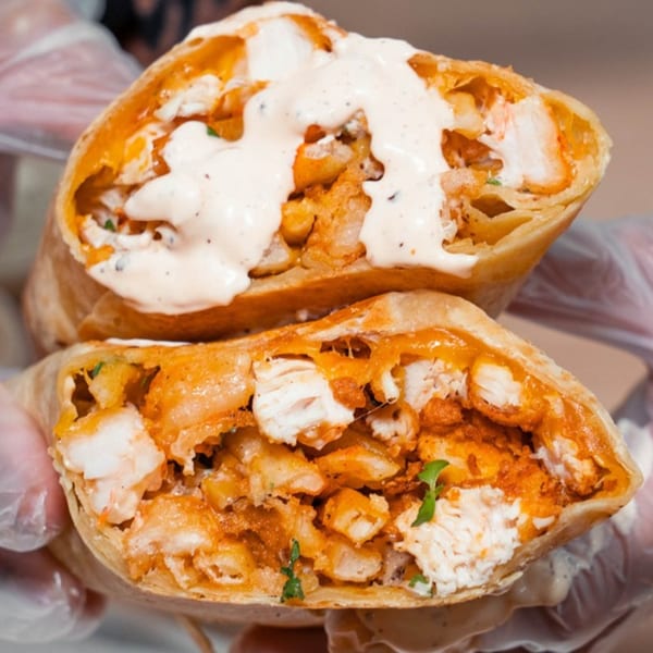 Two halves of a chicken and waffle burrito, filled with chicken, fries, and creamy sauce.