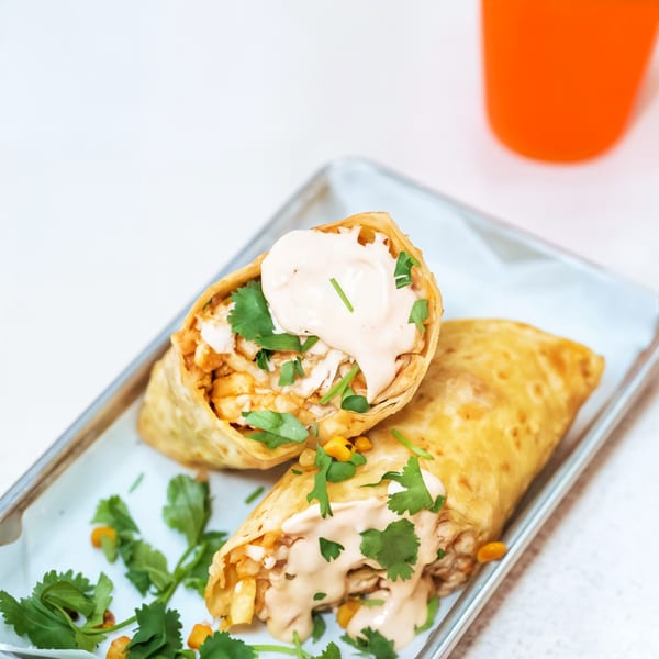 Two chicken and waffle burritos, topped with sauce and cilantro, on a white tray.